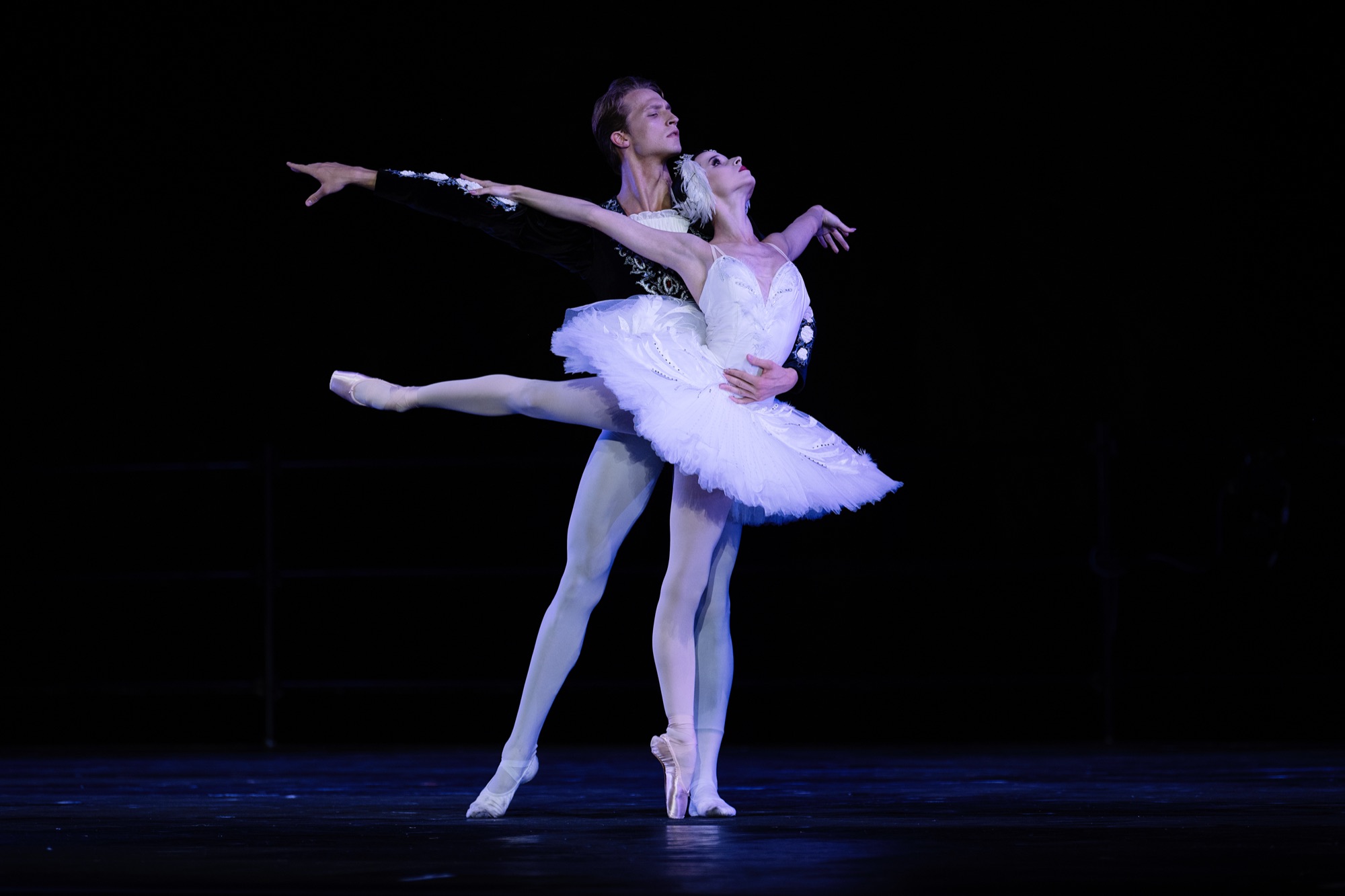A pas de deux on a dark stage, the ballerina in a white tutu