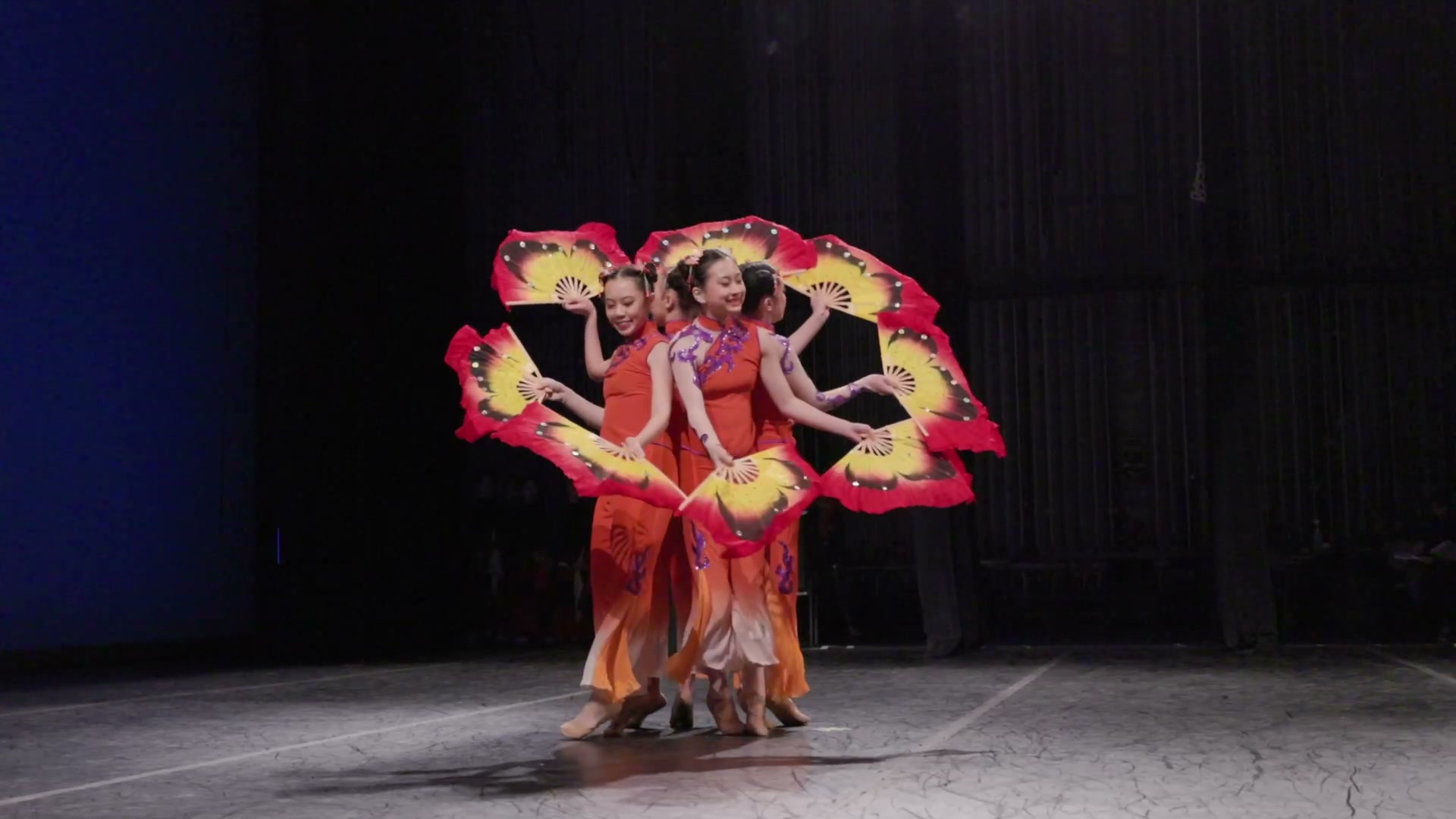 Dancers in red and gold costumes performing a fan dance on stage