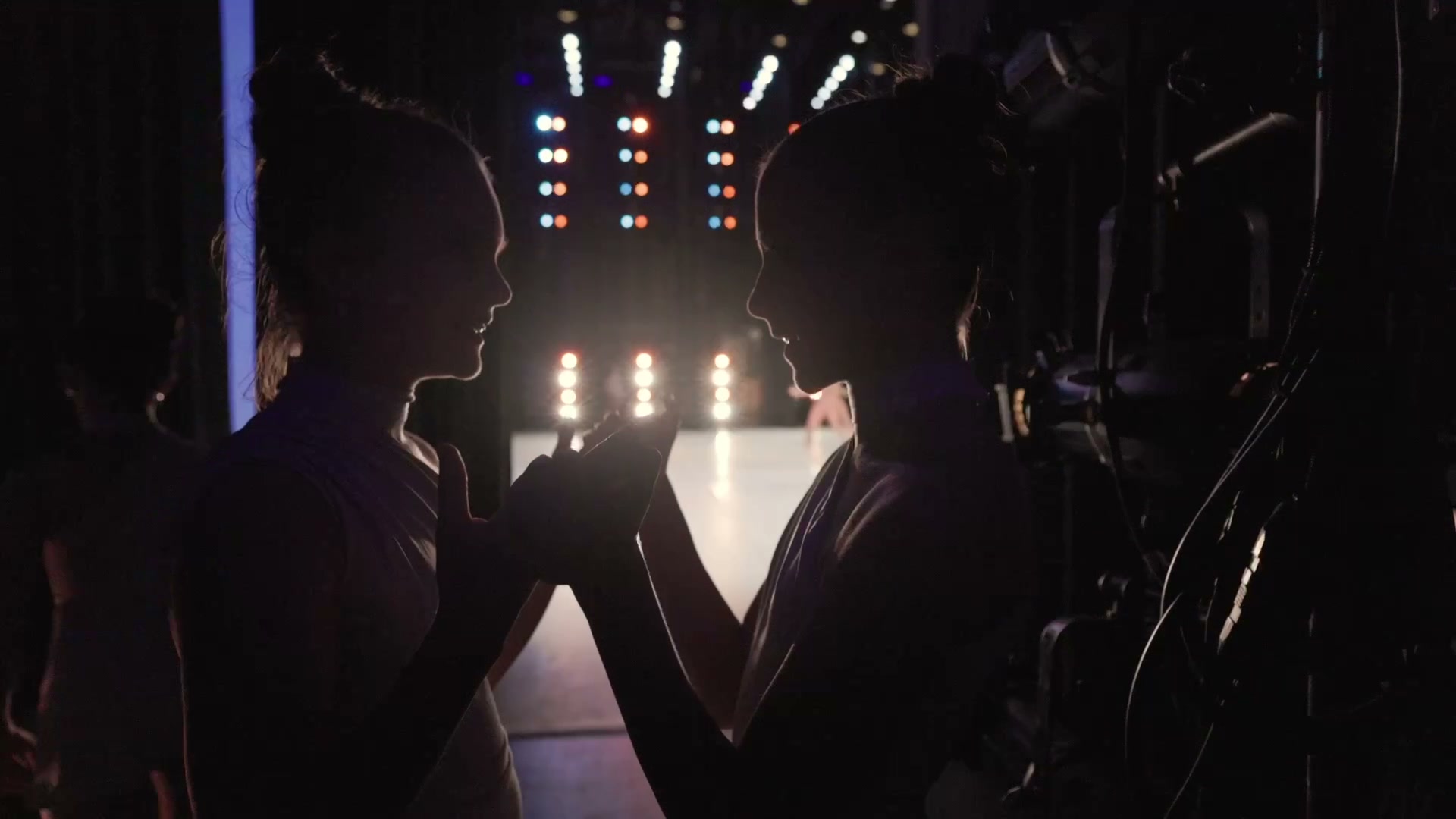Two dancers silhouetted in the wings, holding hands as they wait to go on stage