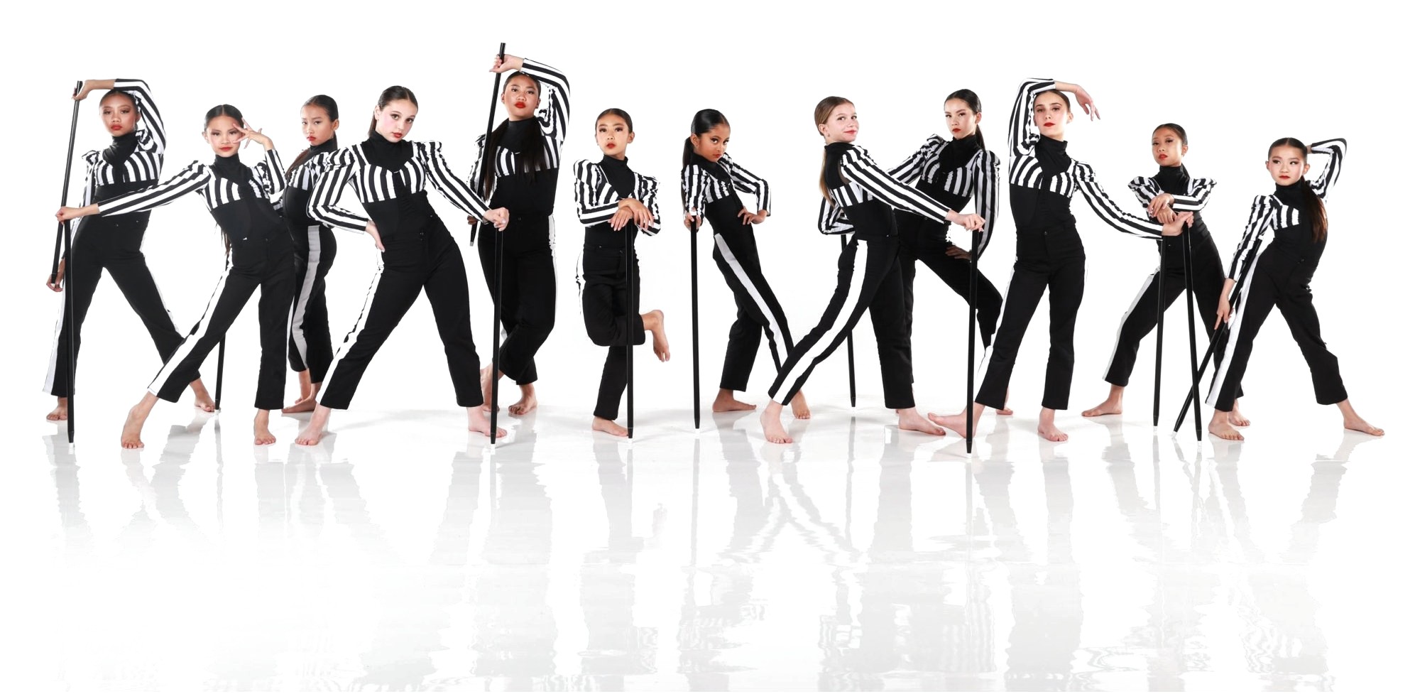 A studio group of young dancers in black and white striped costumes posing with canes on a white set