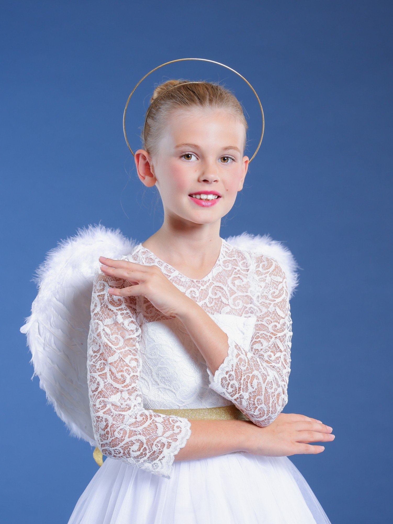 A young dancer dressed as an angel with white wings and a gold halo on a blue backdrop